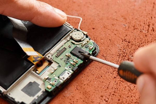 cropped view of professional repairman opening broken cellphone with screwdriver in workshop