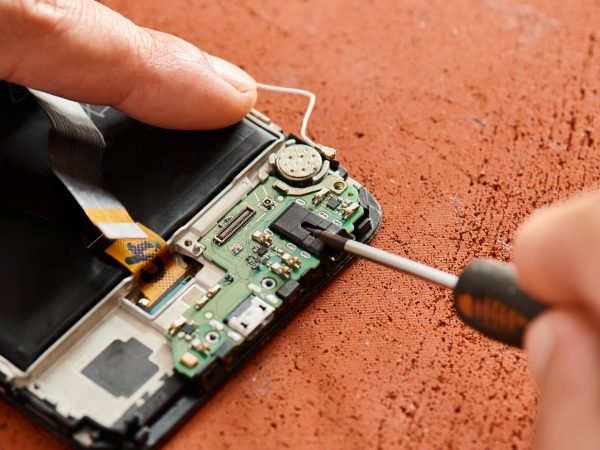 cropped view of professional repairman opening broken cellphone with screwdriver in workshop